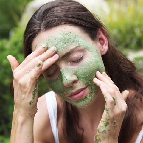 Woman applying a green facial mask.