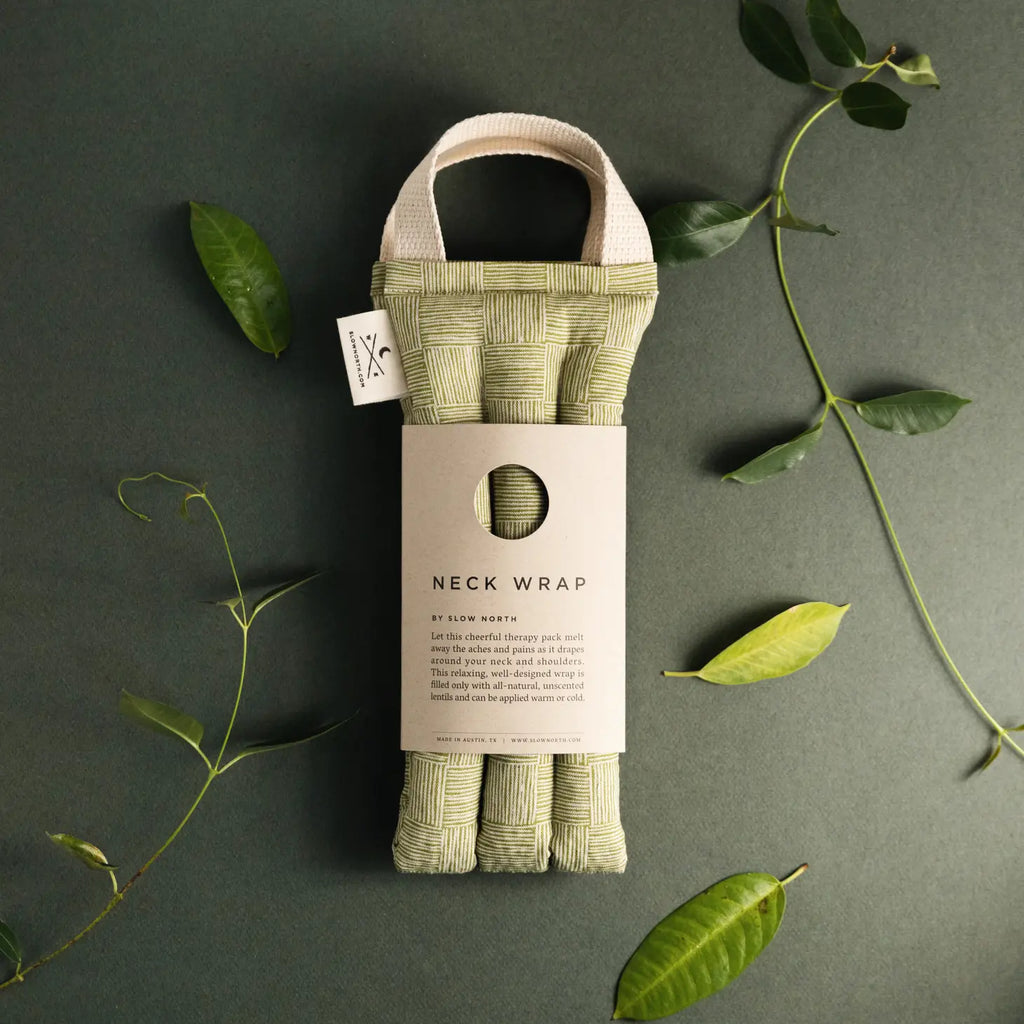 A neck wrap packaged neatly with a label, surrounded by green leaves on a dark background.