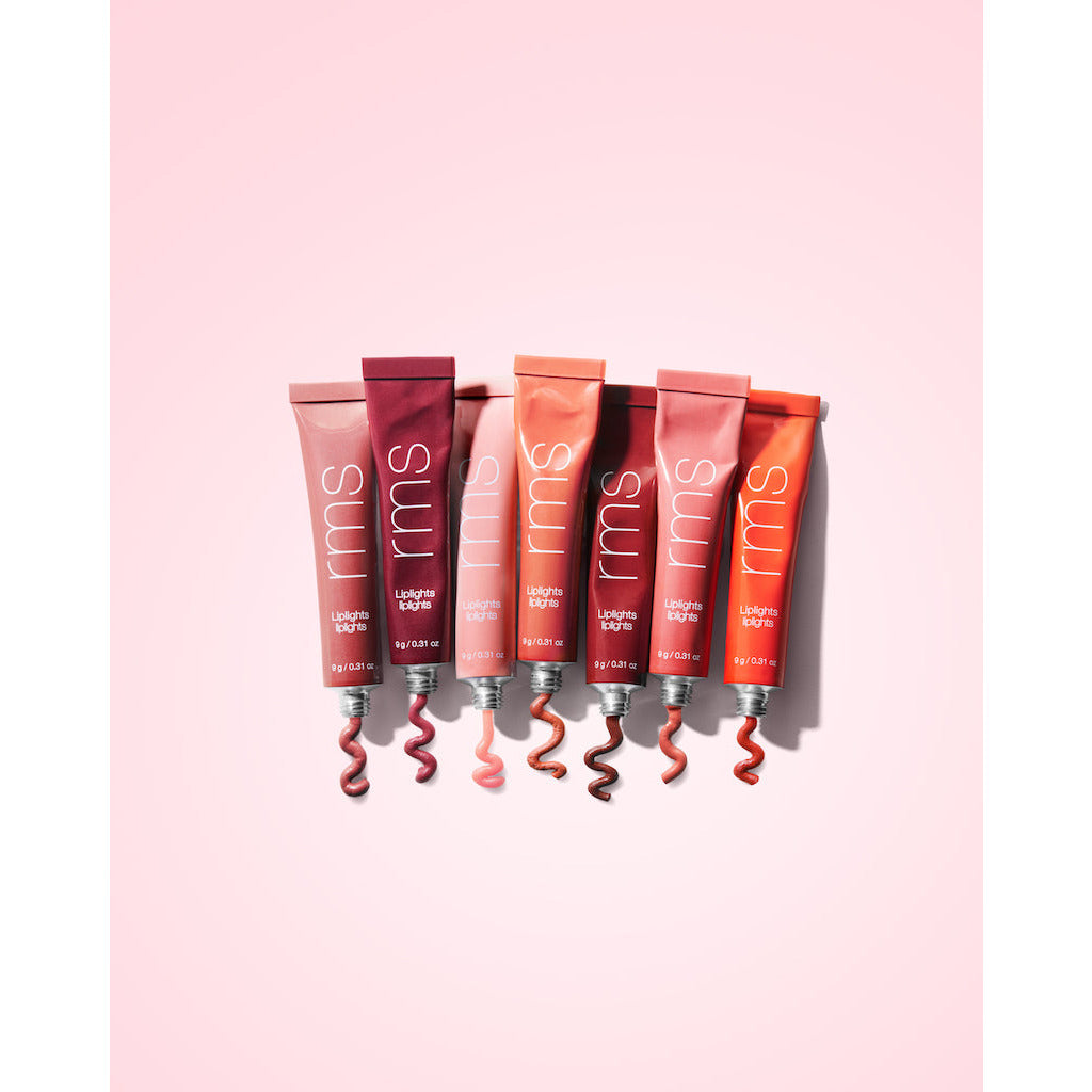 Five tubes of lipstick in various shades with a swatch of each color displayed in front of them on a pink background.