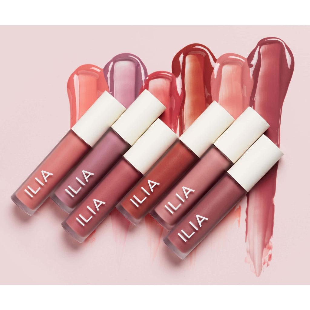 Collection of five ilia brand lip glosses with various shades displayed alongside corresponding color swatches on a pink background.