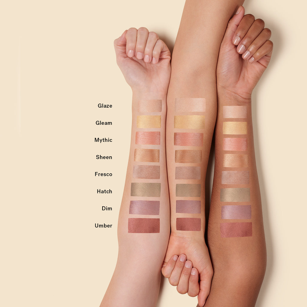 Swatches of various eyeshadow shades on two arms against a beige background.