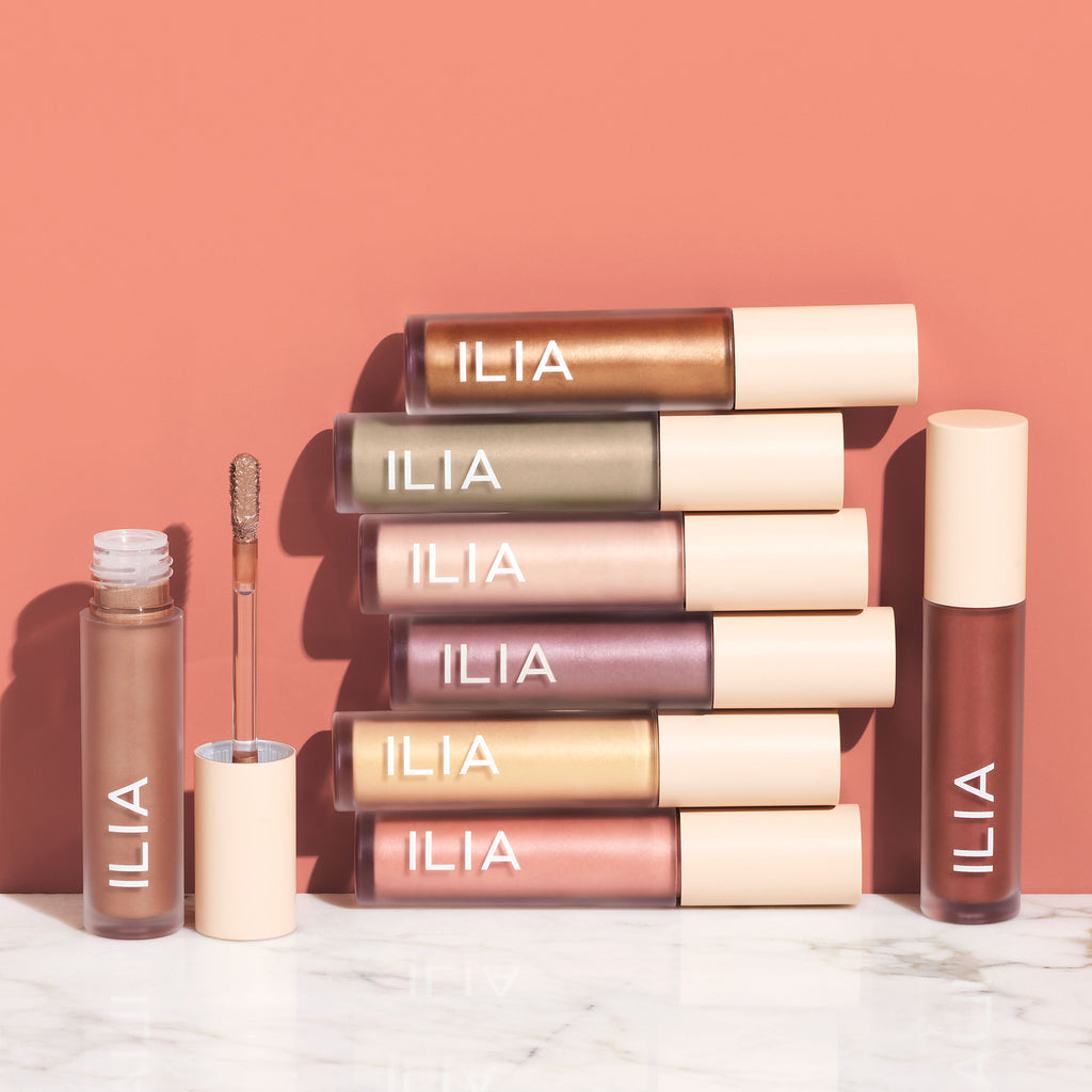 A collection of ilia beauty products arranged neatly against a pink backdrop.