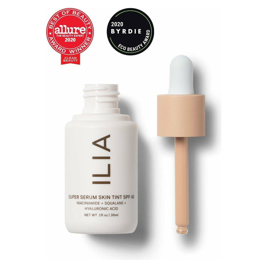 A bottle of ilia super serum skin tint spf 40 with a dropper applicator, along with beauty award badges from allure and byrdie.