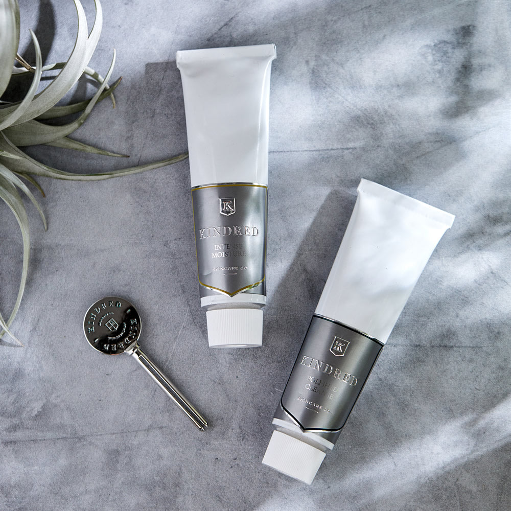 Two tubes of kindred skincare products with a metallic object on a marble surface.