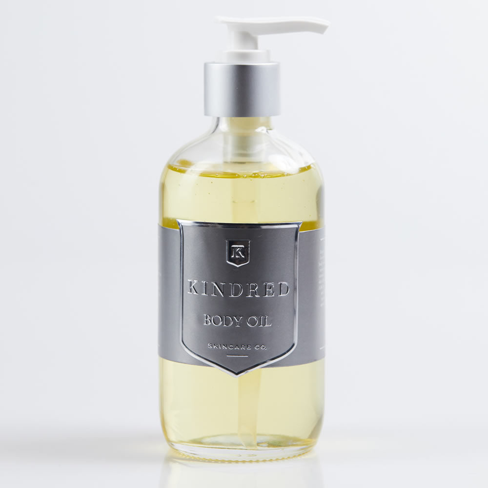 A bottle of kindred body oil with a pump dispenser against a white background.