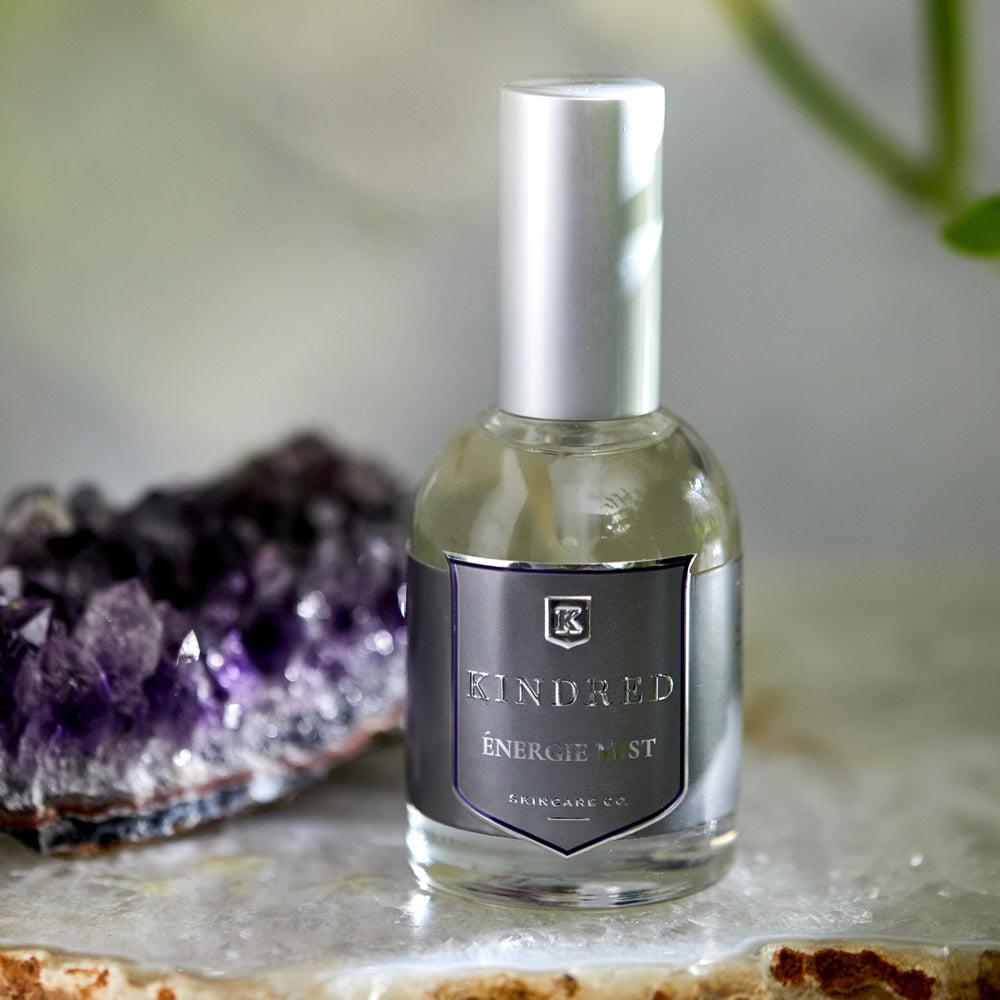 A bottle of kindred energie mist beside an amethyst cluster on a marble surface.