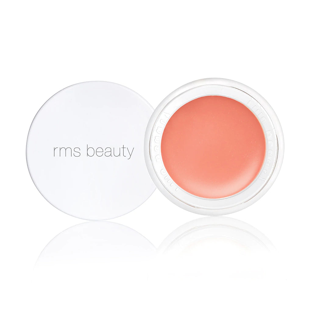 Open container of rms beauty blush with coral-colored product and white lid on reflective surface.