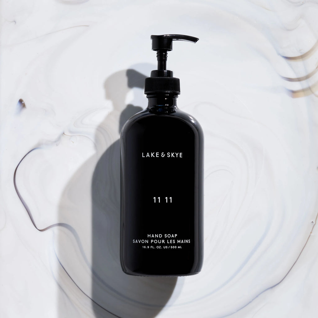 A black hand soap dispenser labeled "lake & skye 11 11" placed on a white surface with shadow patterns.
