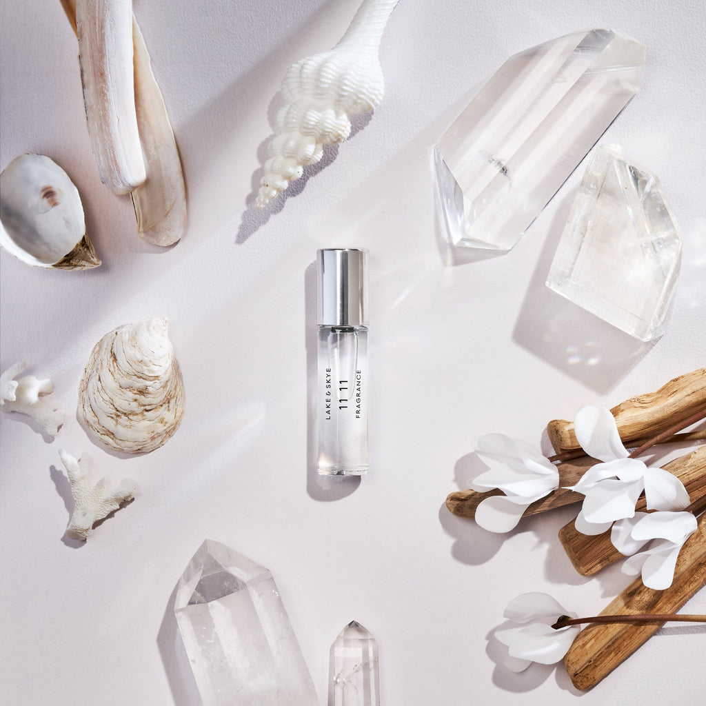 Elegant perfume bottle surrounded by natural elements like shells, crystals, and wooden accents on a bright, textured background.