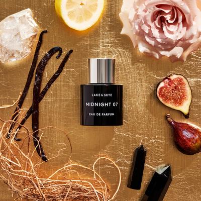A bottle of lake & skye midnight 07 eau de parfum surrounded by natural elements and cosmetic products on a golden background.
