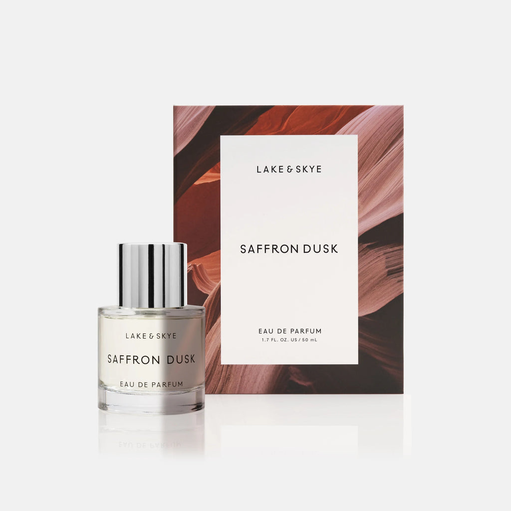 A bottle of lake & skye saffron dusk eau de parfum displayed in front of its packaging with a botanical backdrop.