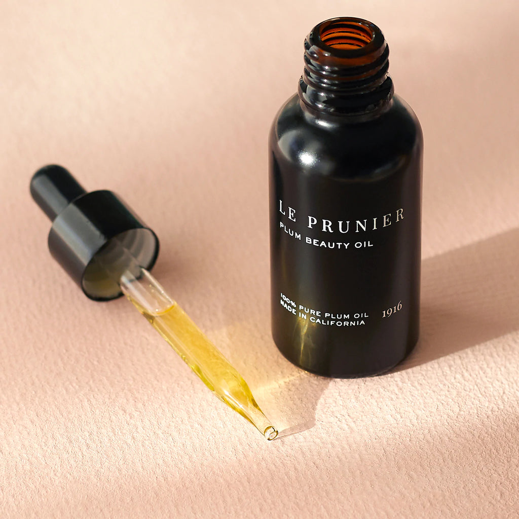 Black bottle of le prunier plum beauty oil with a dropper dispensing oil.