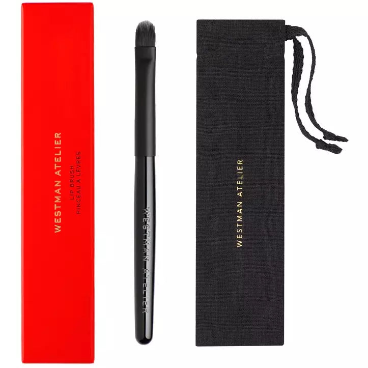 Makeup brush with black handle next to its red packaging and black carrying pouch.