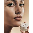 Woman holding a cosmetic product near her face.