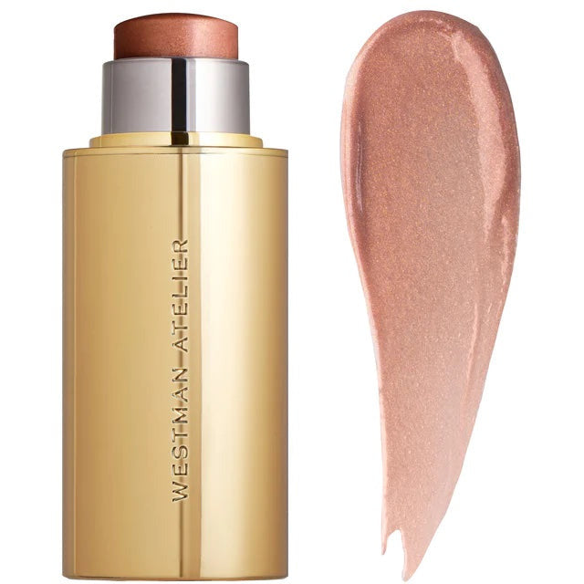 A swatch of creamy highlighter beside its gold packaging.