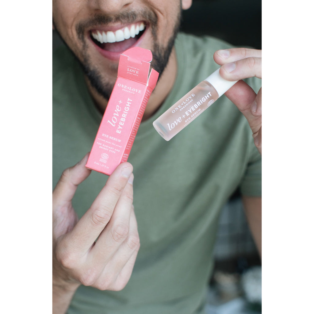 A smiling person holding a tube and applicator of love beauty lip balm.