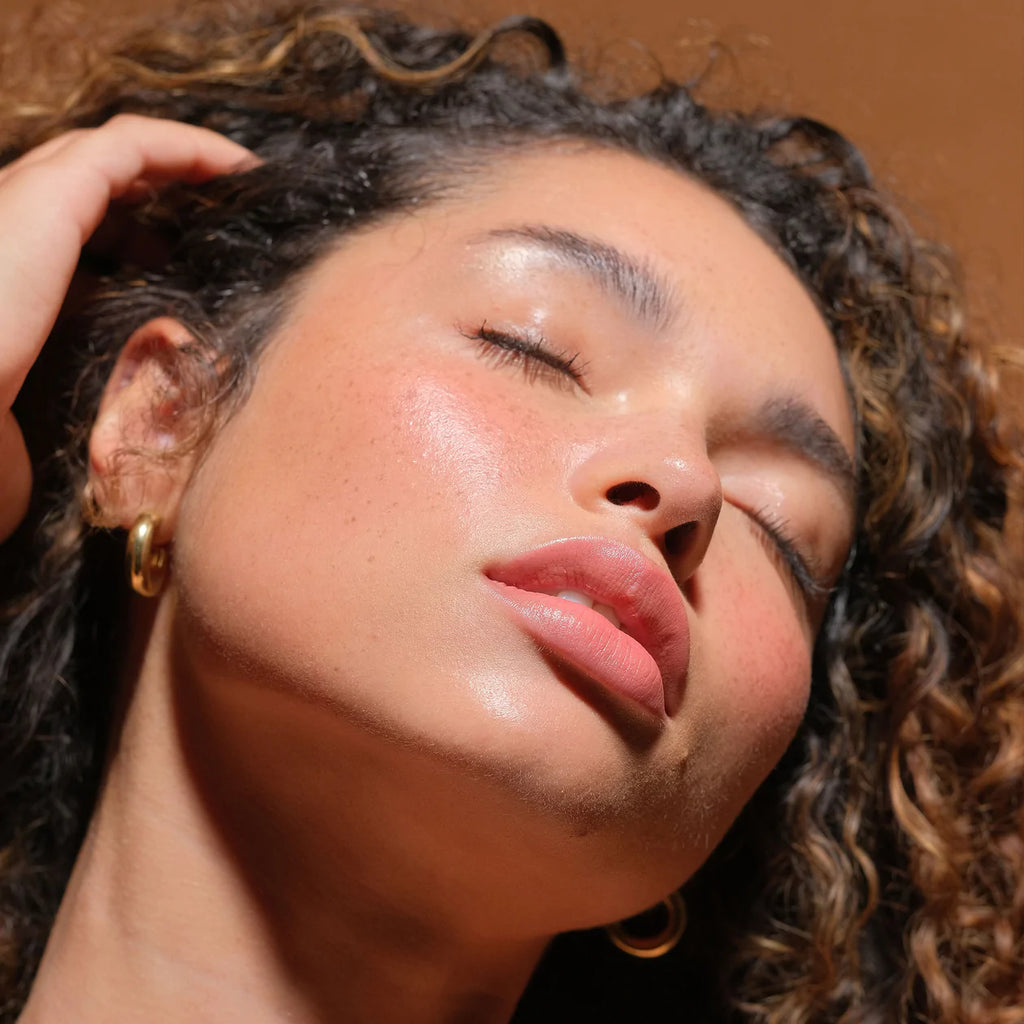 Close-up of a woman with curly hair enjoying warmth, highlighting her glowing skin and closed eyes.