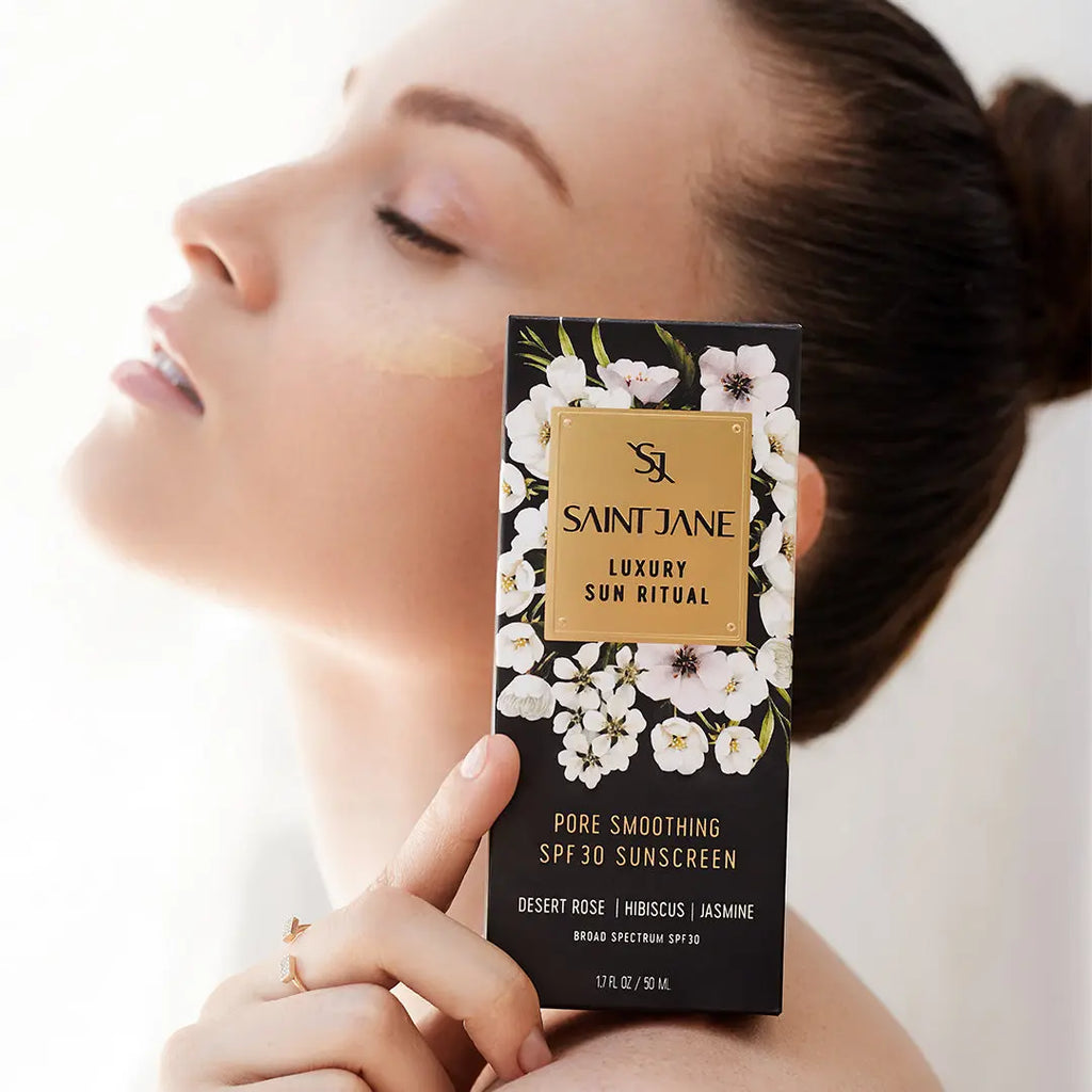 Woman holding a product called "saint jane luxury sun ritual spf 30 sunscreen" with a serene expression.