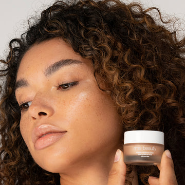 Woman holding a beauty cream jar next to her face.