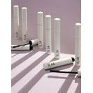 A collection of white mascara tubes with brushes placed on a surface with a purple and white striped pattern.