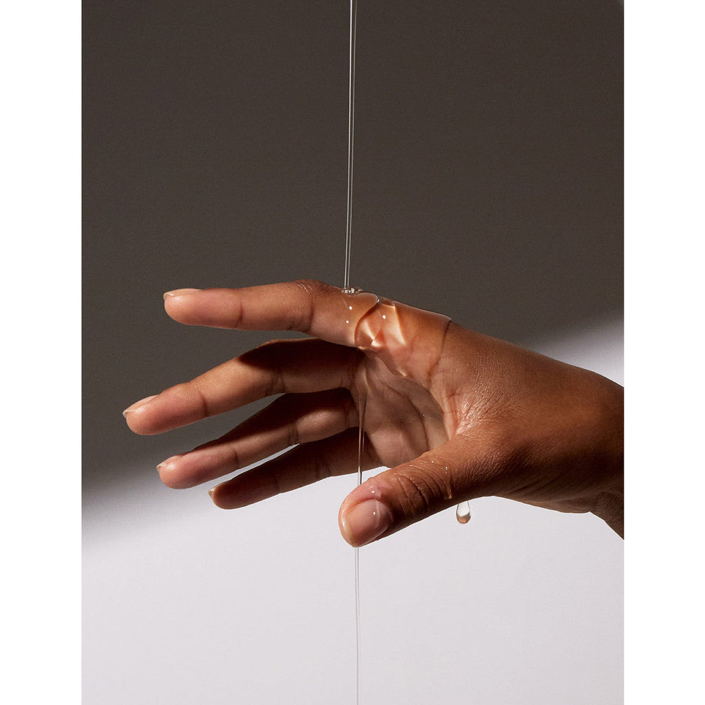 Hand interacting with a thin stream of viscous liquid against a neutral background.