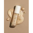Liquid foundation bottle with makeup smears on a beige background.