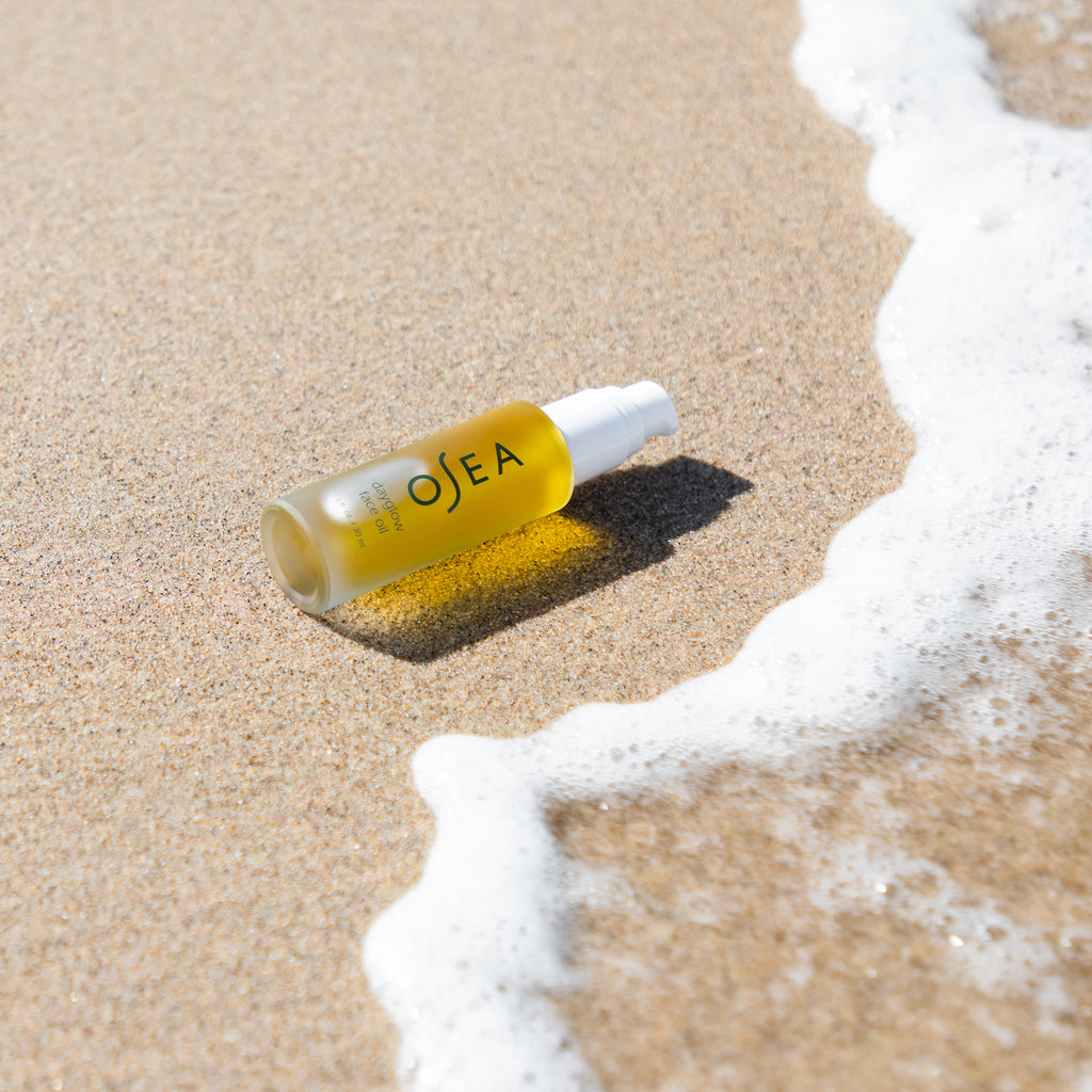 A bottle of osea skincare product lying on sandy beach with an approaching wave.