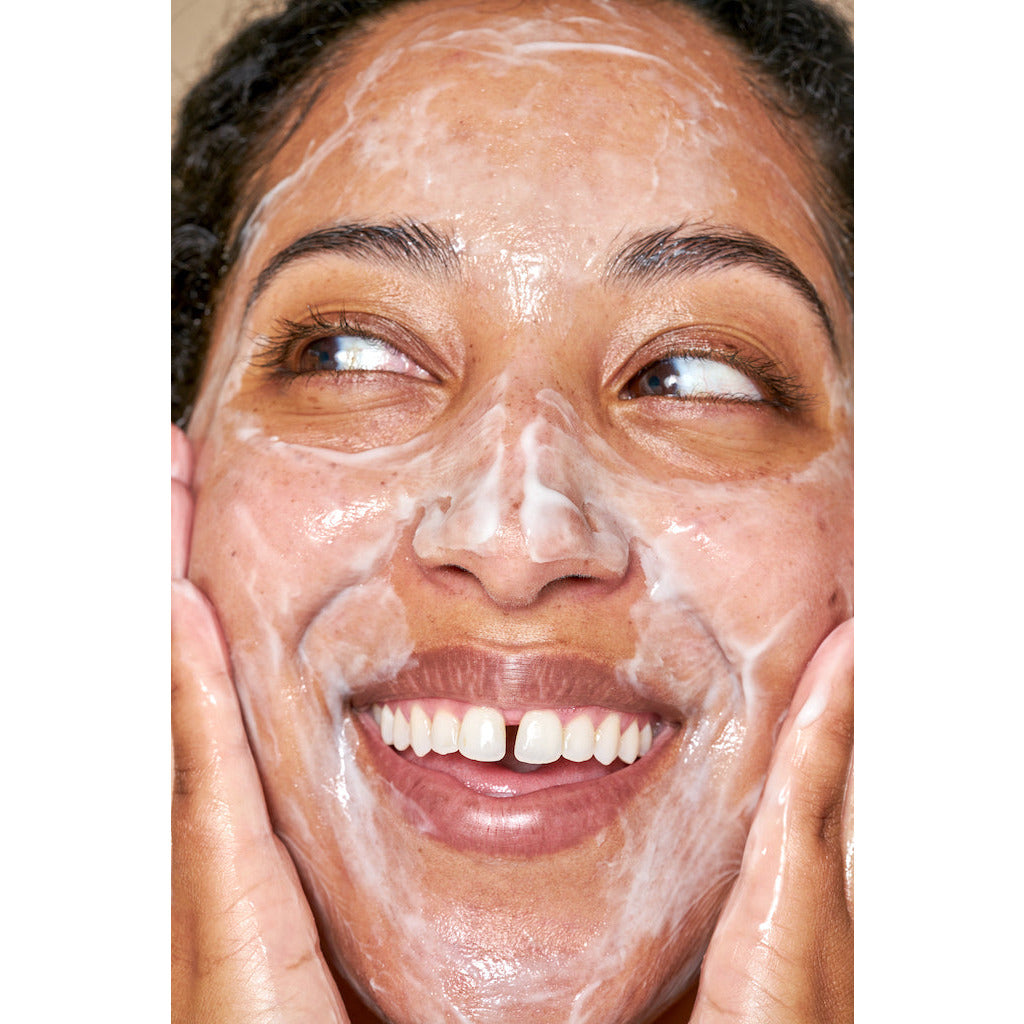 Woman with a facial cleanser applied on her skin, smiling and looking upwards.