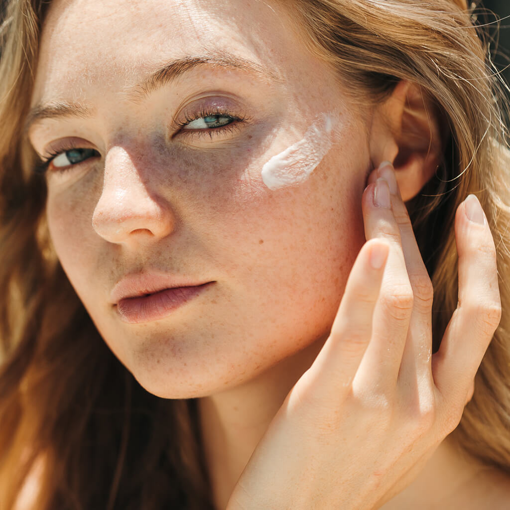 A woman applying sunscreen to her cheek.