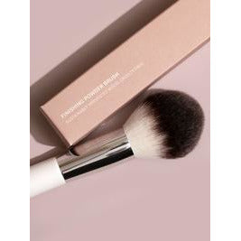A makeup brush positioned against a matching pink background.