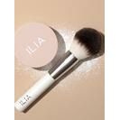 Makeup brush with powder and brand name "ilia" visible.