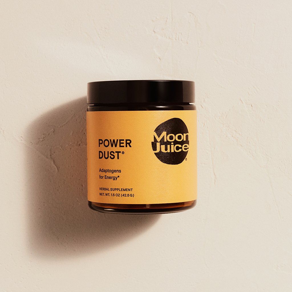 A jar of moon juice power dust herbal supplement against a textured wall.