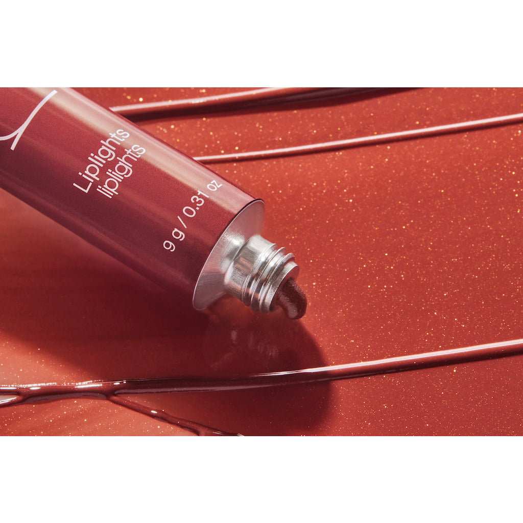 A tube of liquid lipstick with product oozing out, placed on a shiny red surface.