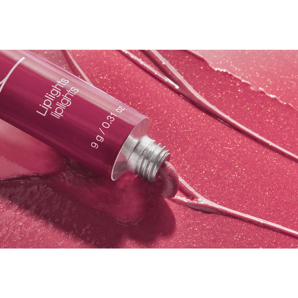 A squeezed tube of lip gloss on a glossy, shimmering surface with the product spilled out.