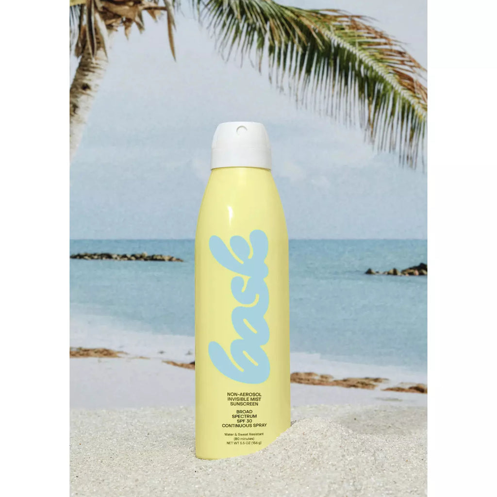 A yellow sunscreen spray bottle on a beach background with clear skies and palm leaves.