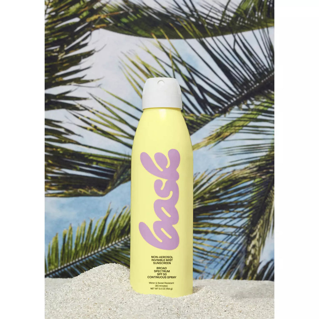 A spray can labeled "back" placed on a sandy surface with palm leaves and a blue sky in the background.