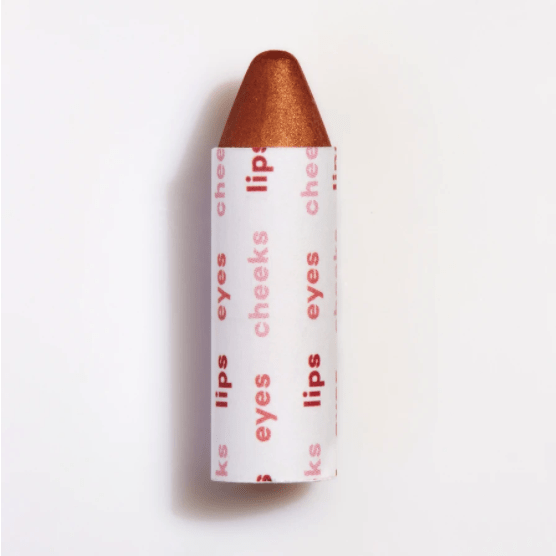 A single lipstick with a rose gold cap and casing labeled with words "eyes cheeks lips" on a plain background.