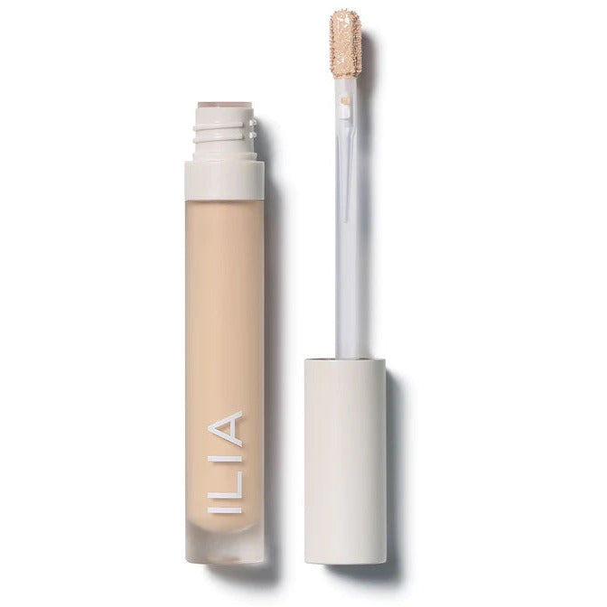 A bottle of liquid concealer next to its applicator wand on a white background.