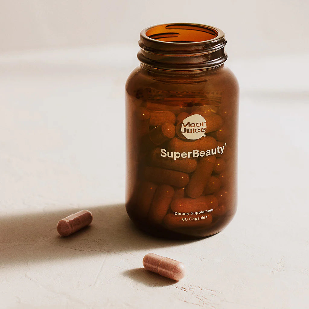 Amber glass bottle labeled "superbeauty" with capsules, two of which are outside the container, on a neutral surface.