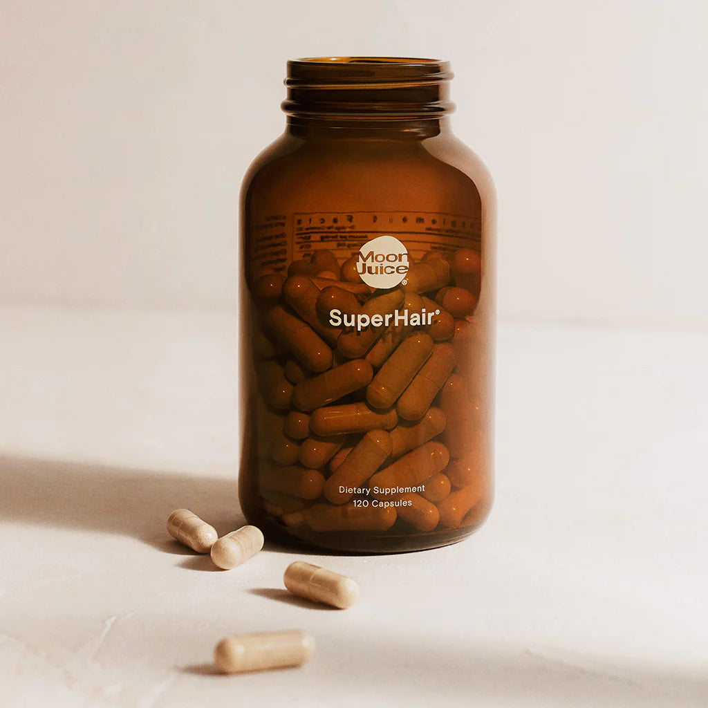 A jar of "superhair" dietary supplement capsules with some capsules spilled out onto a surface.