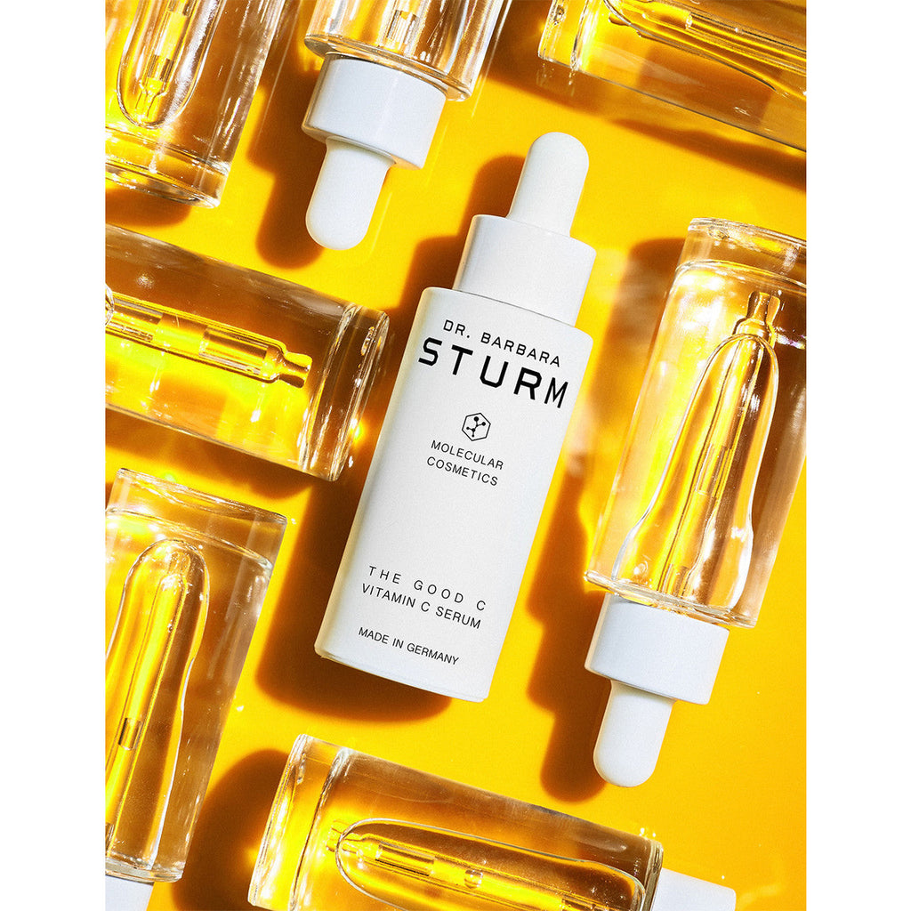 A bottle of dr. barbara sturm vitamin c serum surrounded by droppers on a vibrant yellow background.