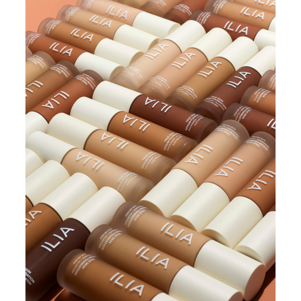 An array of cosmetic foundation sticks in various shades displayed in a pattern against an orange background.