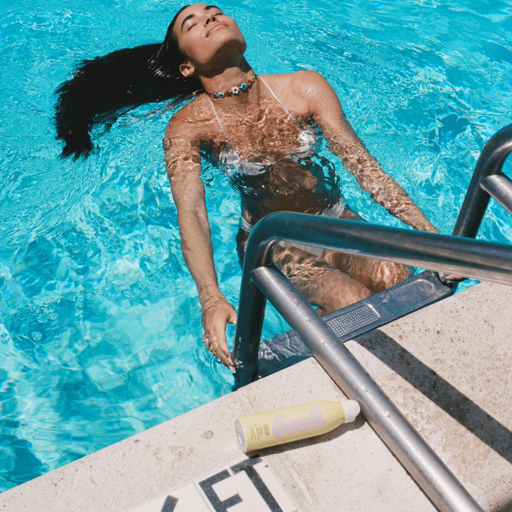 Woman relaxing in a swimming pool near the steps, with sunscreen on the edge.
