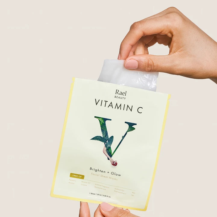 A hand holding a rael beauty vitamin c facial sheet mask package against a neutral background.