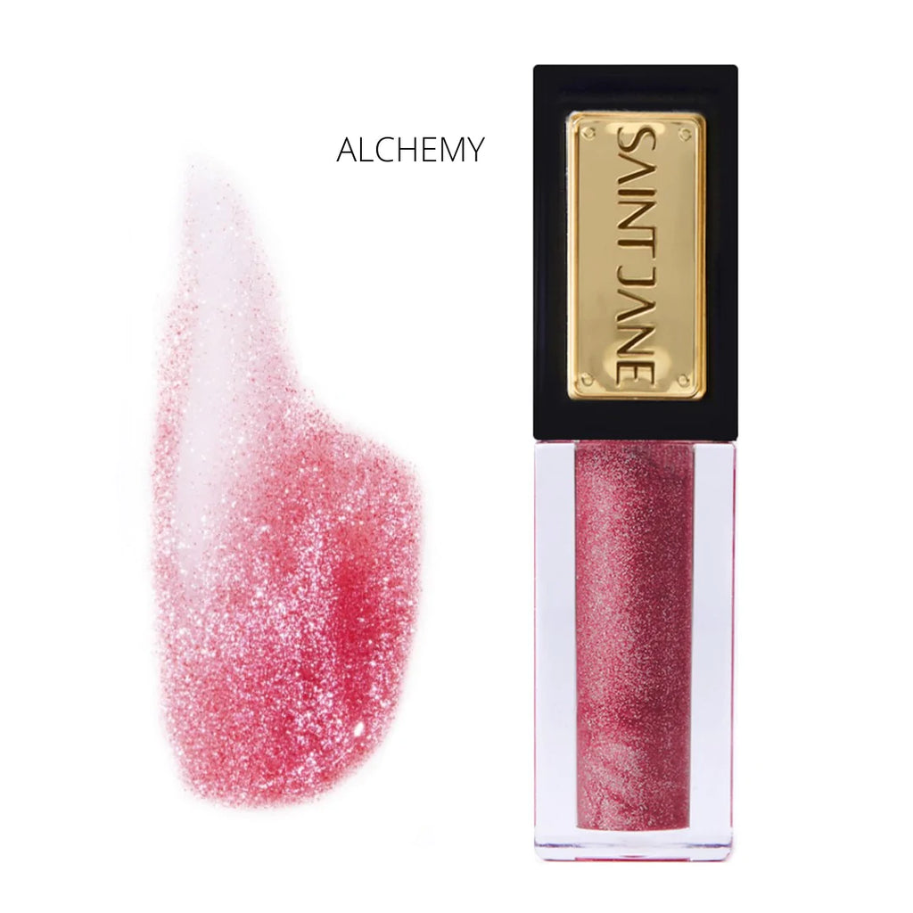 A swatch of shimmering reddish-pink lipstick next to its corresponding tube labeled "saint jane - alchemy".