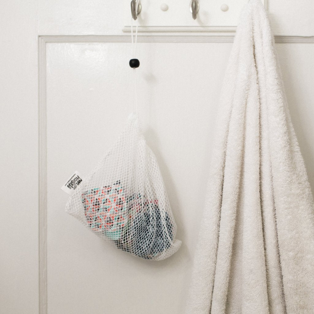 A mesh laundry bag filled with clothes hanging next to a towel on a white door.