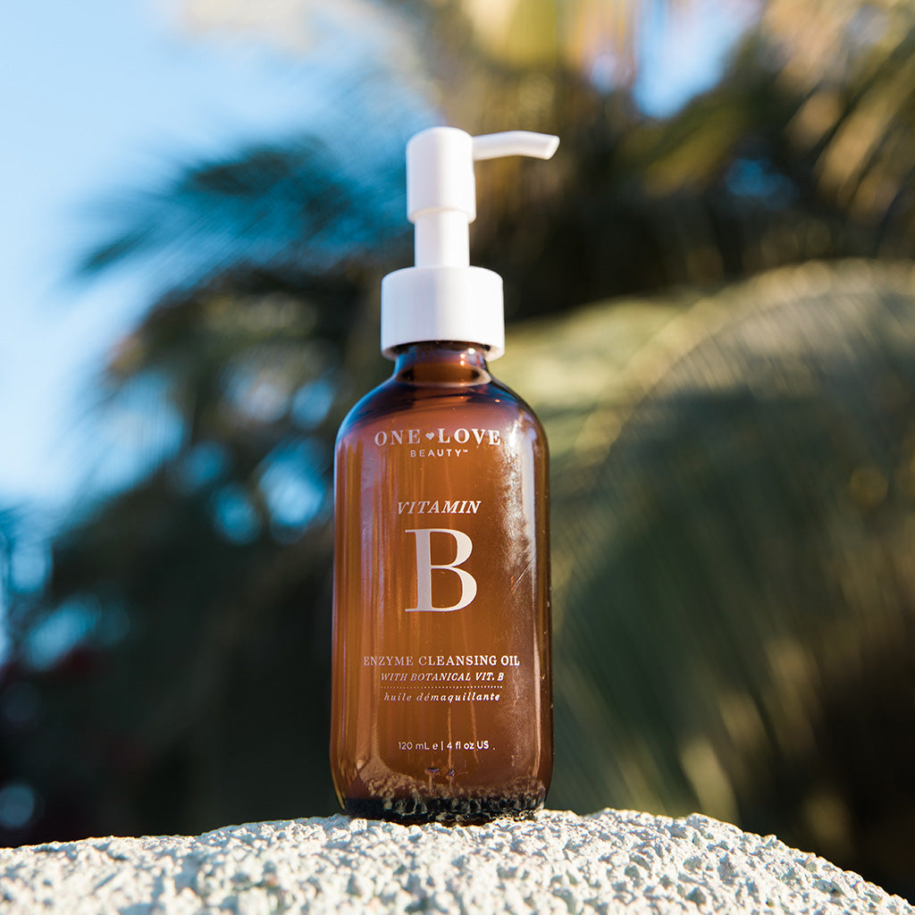Bottle of vitamin b enzyme cleansing oil with tropical palm leaves in the background.