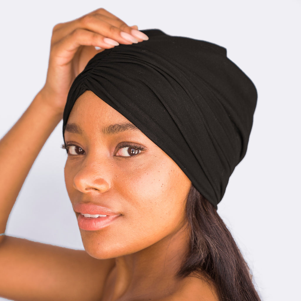 Woman wearing a black headwrap with a gentle hand pose.