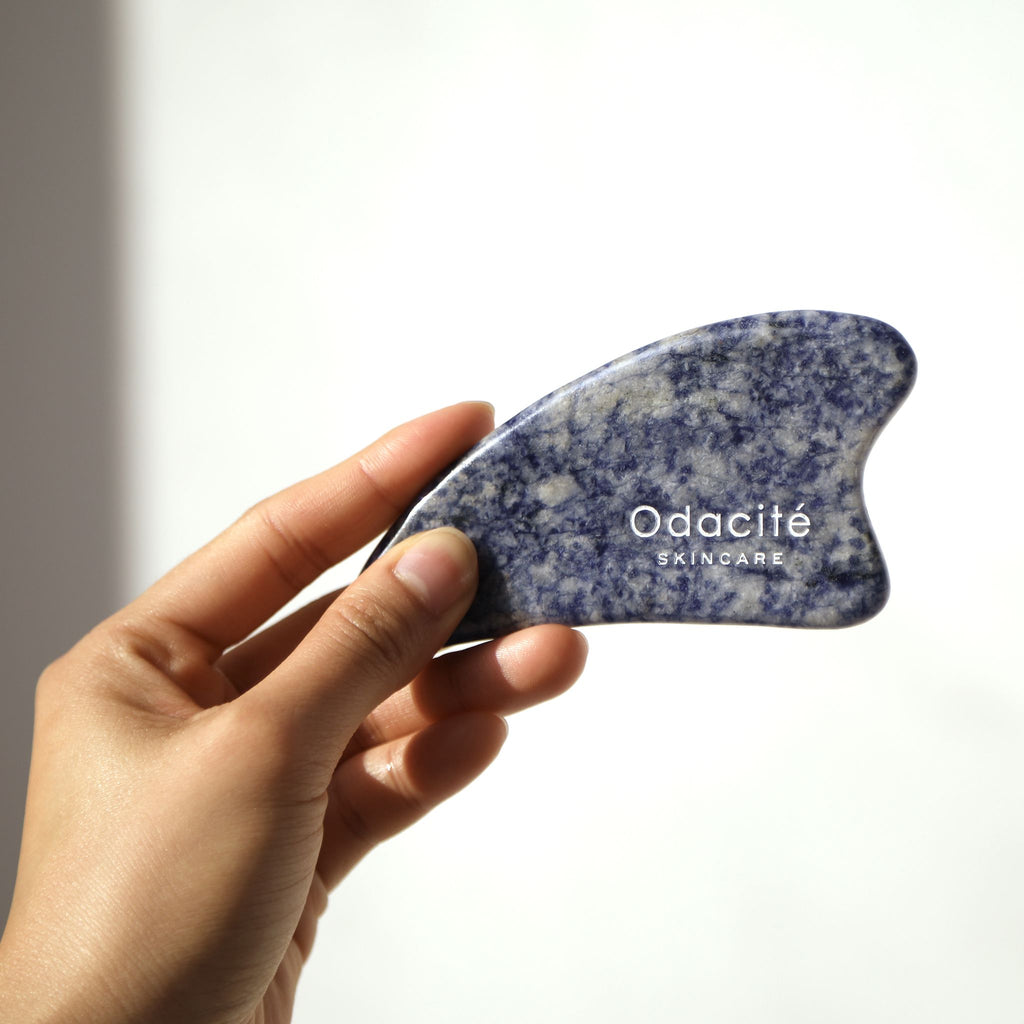 A hand holding a blue odacite branded skincare tool against a light background.