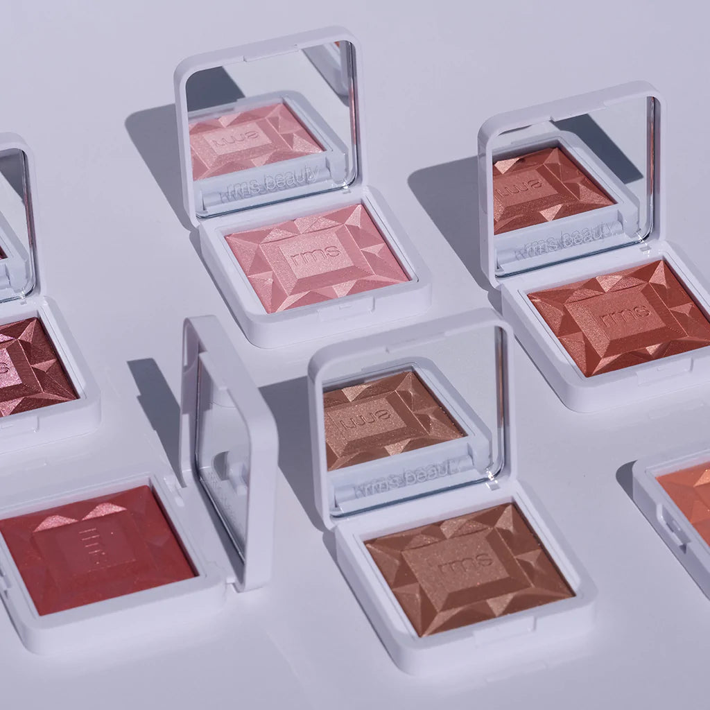 A collection of open cosmetic blush compacts in various shades arranged on a surface.